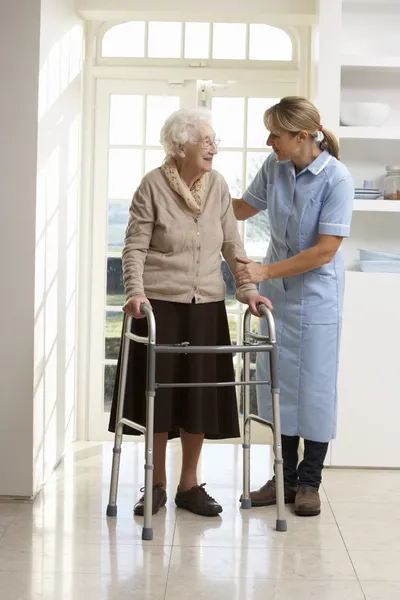 Opiekun pomaga podeszłym wieku starszy kobieta za pomocą balkonik — Zdjęcie stockowe