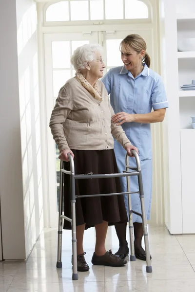 Φροντιστής βοηθώντας ηλικιωμένη γυναίκα ανώτερος που χρησιμοποιώντας το πλαίσιο με τα πόδια — Φωτογραφία Αρχείου