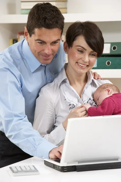 Родители с новорожденным ребенком работают из дома с помощью ноутбука — стоковое фото