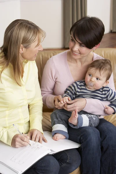 Mãe com bebê conversando com visitante de saúde em casa — Fotografia de Stock