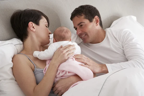 Pais abraçando o bebê recém-nascido na cama em casa — Fotografia de Stock
