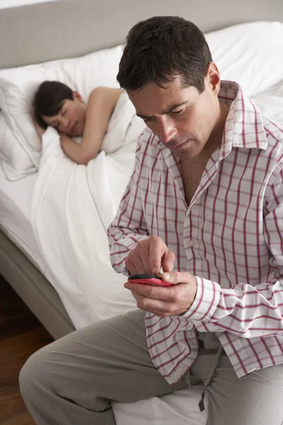 Podezíravý manžel kontrola manželky mobilní telefon, zatímco ona spí — Stock fotografie