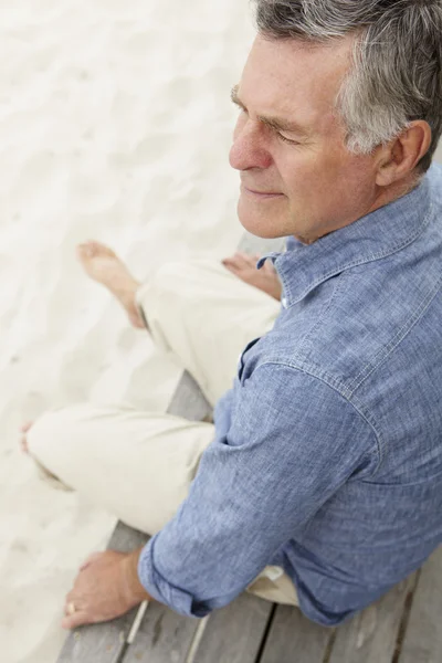 Старший мужчина, сидящий на пляже — стоковое фото