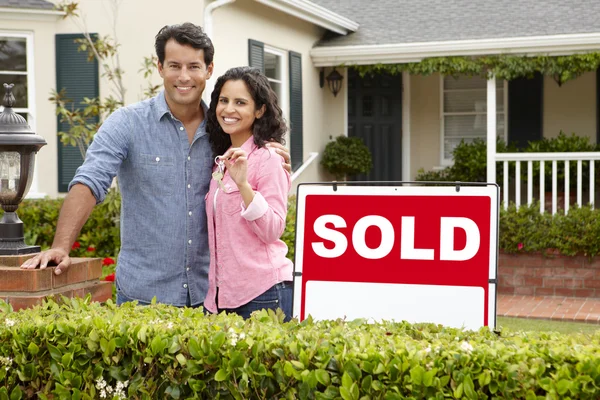 Hispanic couple outside home with sold sign — Stock Photo, Image