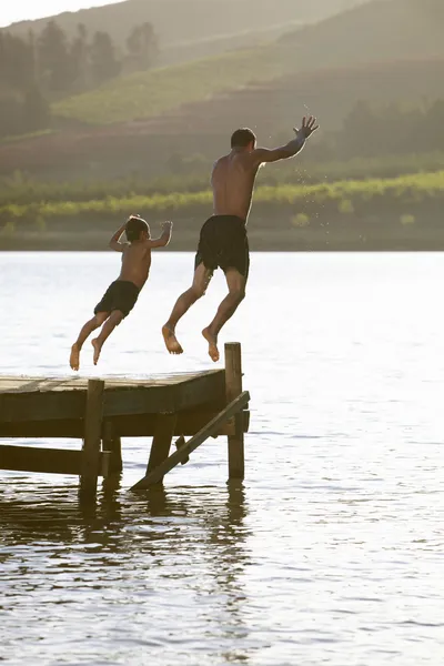 Молодой человек с ребенком прыгает в воду — стоковое фото
