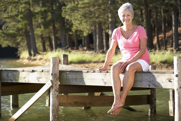 Пожилая женщина, сидящая у озера — стоковое фото