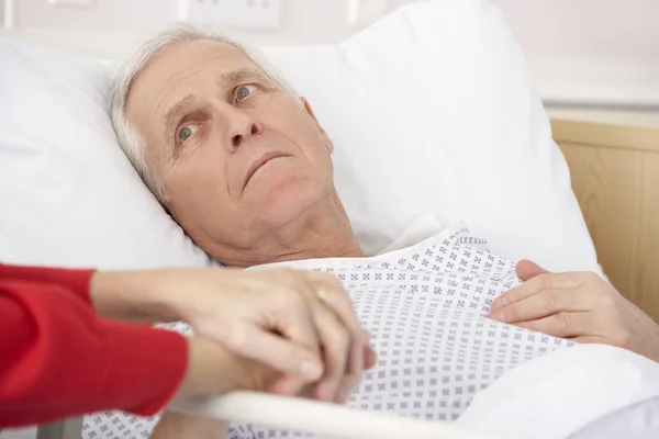 Hombre mayor en cama de hospital sosteniendo la mano de la esposa — Foto de Stock