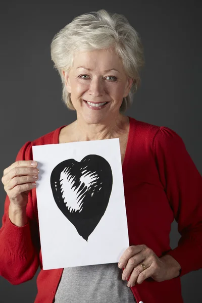 Mulher sênior segurando tinta desenho do coração — Fotografia de Stock