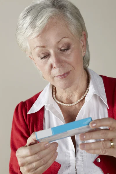 Старшая женщина смотрит рецепт упаковки наркотиков — стоковое фото