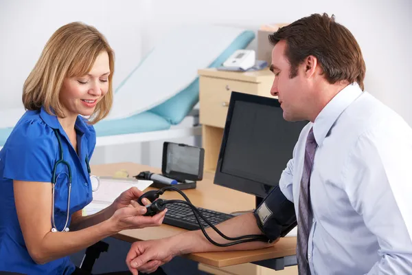 UK médico tomando a pressão arterial do paciente — Fotografia de Stock