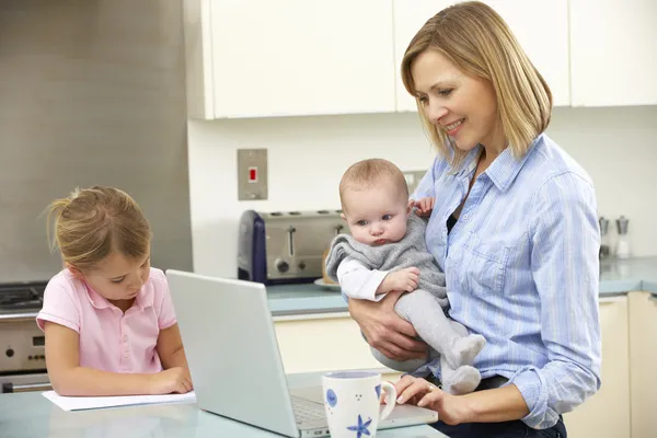 Matka s dětmi používat přenosný počítač v kuchyni — Stock fotografie