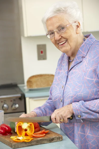 Старшая женщина режет овощи на домашней кухне — стоковое фото