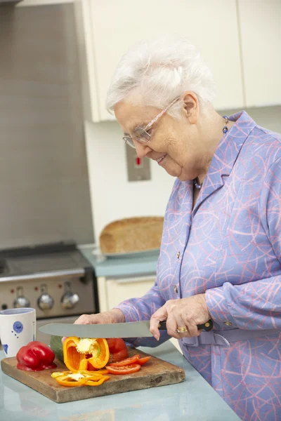 Mulher sênior cortando legumes na cozinha doméstica — Fotografia de Stock