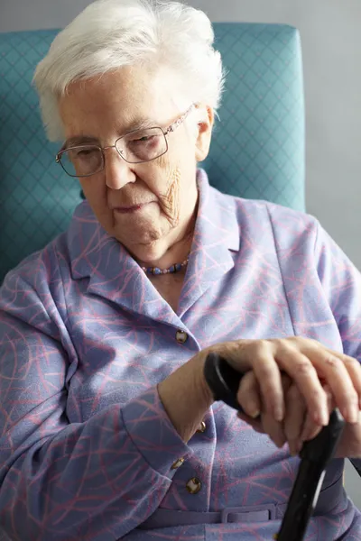 Mulher Senior infeliz sentada na cadeira segurando a bengala — Fotografia de Stock