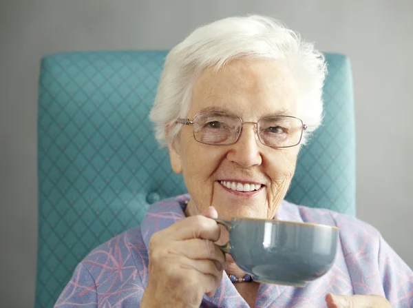 Äldre kvinna avkopplande i stol med varm dryck — Stockfoto