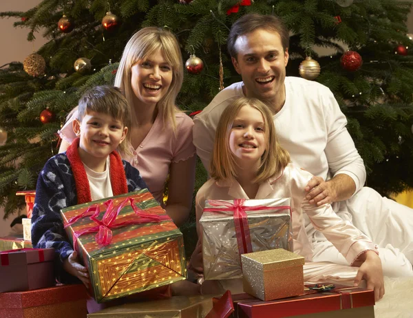 Familia abriendo regalo de Navidad delante del árbol Imágenes de stock libres de derechos