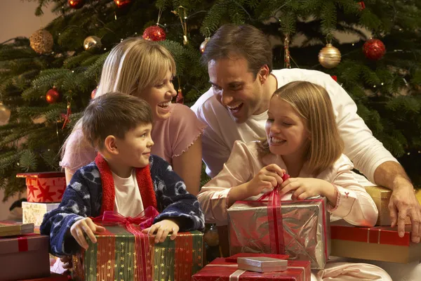 Familj öppnar julklapp framför trädet Stockbild
