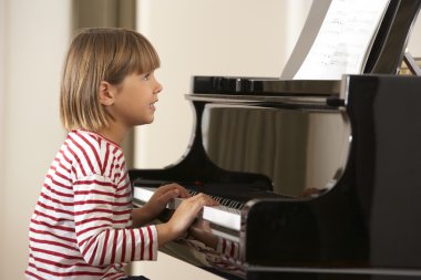 Young girl playing grand piano at home clipart