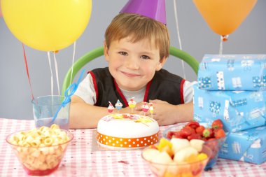 Young boy with birthday cake and gifts at party clipart