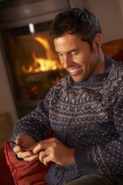 Middle Aged Man Using MP3 Player By Cosy Log Fire clipart