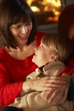 Mother And Daughter Relaxing On Sofa By Cosy Log Fire clipart