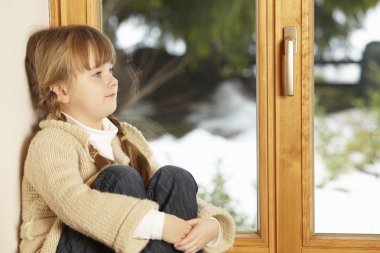 Young Girl Sitting On Window Ledge Looking At Snowy View clipart