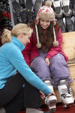 Sales Assistant Helping Teenage Girl To Try On Ski Boots In Hire clipart