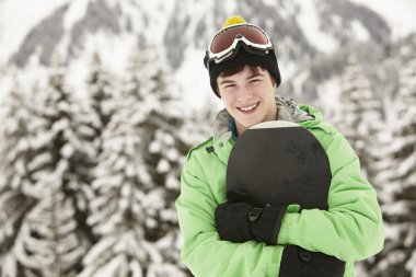 Teenage Boy With Snowboard On Ski Holiday In Mountains clipart