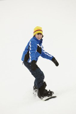 Young Boy Snowboarding Down Slope On Holiday In Mountain clipart