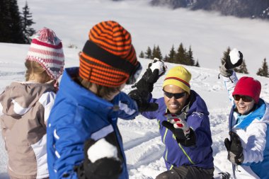 Family Having Snowball Fight On Ski Holiday In Mountains clipart