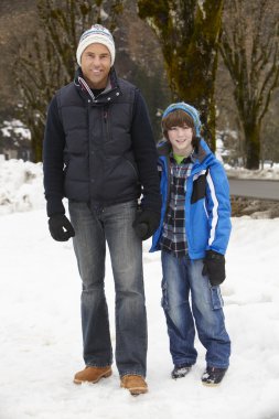 Father And Son Walking Along Snowy Street In Ski Resort clipart