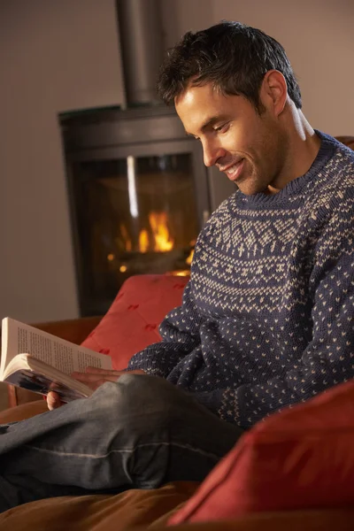 Średniej wieku człowiek relaks z książką przez przytulnym kominkiem — Zdjęcie stockowe