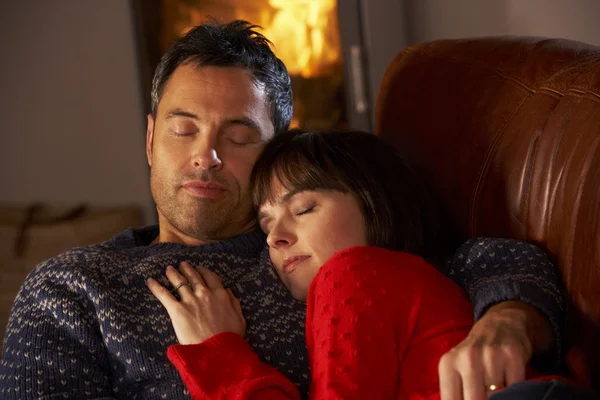 Middle Aged Couple Cuddling On Sofa By Cosy Log Fire — Stock Photo, Image