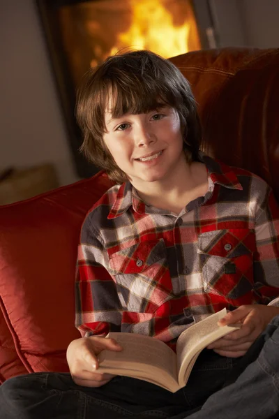 Giovane ragazzo rilassante con libro da accogliente log fuoco — Foto Stock