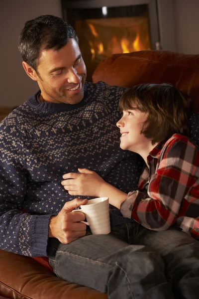 Father And Son Relaxing With Hot Drink By Cosy Log Fire — Zdjęcie stockowe