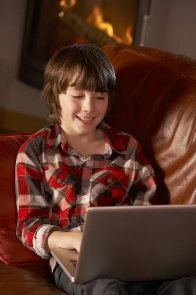 Młody chłopak relaksujący z laptopa przez przytulnym kominkiem — Zdjęcie stockowe