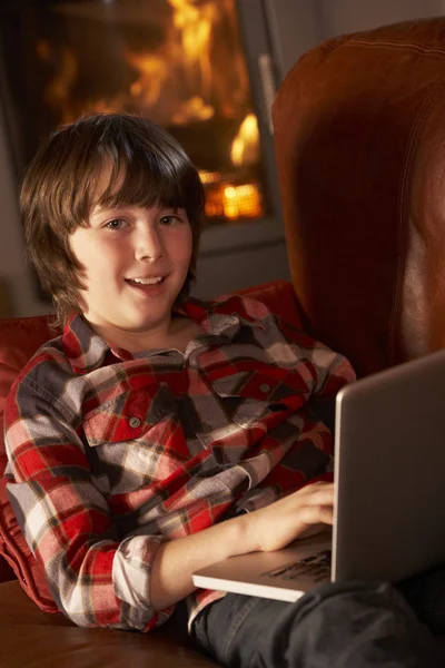 Giovane ragazzo rilassante con computer portatile da accogliente log fuoco — Foto Stock