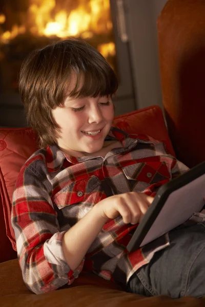 Chico joven que relaja con la computadora de la tableta por el fuego acogedor del registro — Foto de Stock