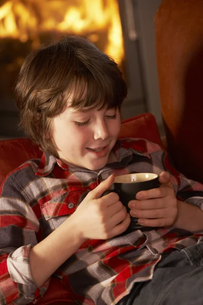 Giovane ragazzo rilassante con bevanda calda da accogliente log fuoco — Foto Stock