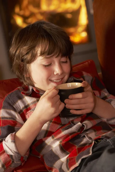 Genç çocuk rahat rahat günlük ateş tarafından sıcak bir içecek ile — Stok fotoğraf