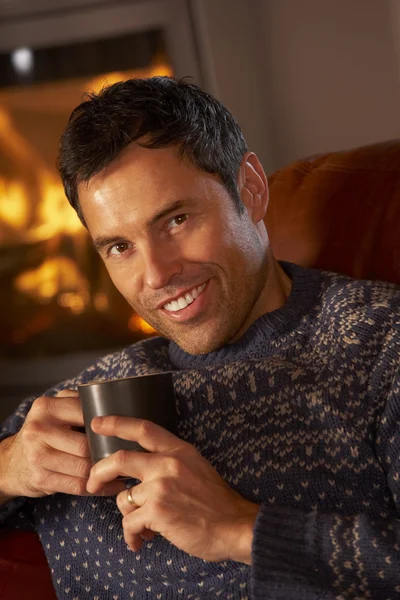 Middle Aged Man Relaxing With Hot Drink By Cosy Log Fire — Stock Photo, Image