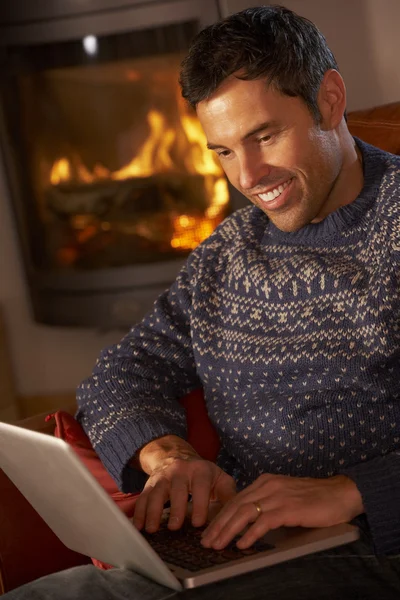 Среднего возраста человек с помощью ноутбука компьютер, уютный огонь журнала — стоковое фото