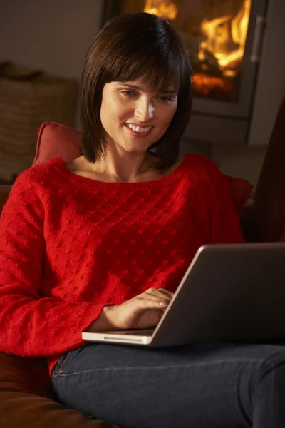 Midden leeftijd vrouw laptopcomputer gebruikt door gezellige open haard — Stockfoto