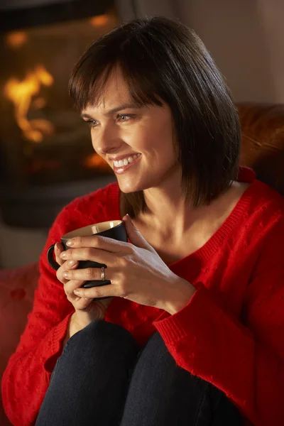 Frau mittleren Alters entspannt sich mit Heißgetränk am gemütlichen Kaminfeuer — Stockfoto
