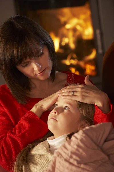 Mor tröstande sjuka dotter på soffan av mysiga logg brand — Stockfoto
