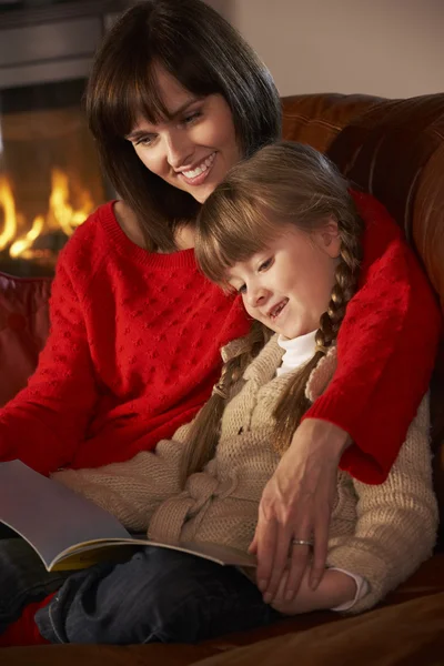 Dcera a matka seděla na pohovce a čtení knihy do útulné log — Stock fotografie
