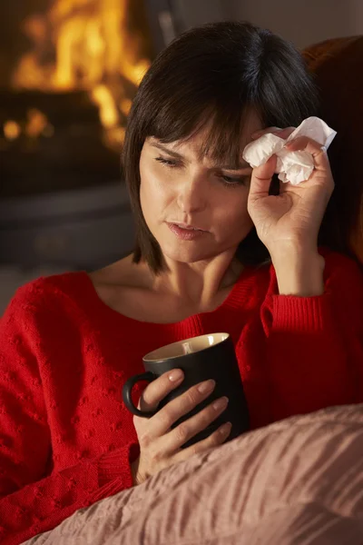 Chora kobieta z zimną odpoczynku na kanapie przy przytulnym kominkiem — Zdjęcie stockowe