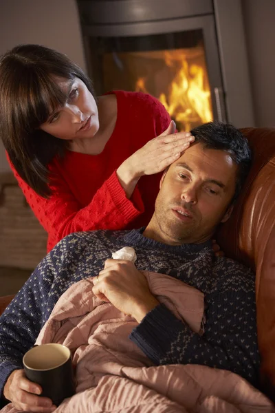 Hustru omvårdnad sjuk man med kall vila på soffan av mysiga log — Stockfoto