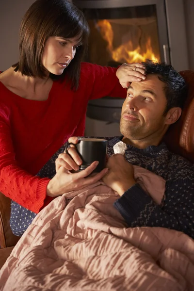 Hustru omvårdnad sjuk man med kall vila på soffan av mysiga log — Stockfoto