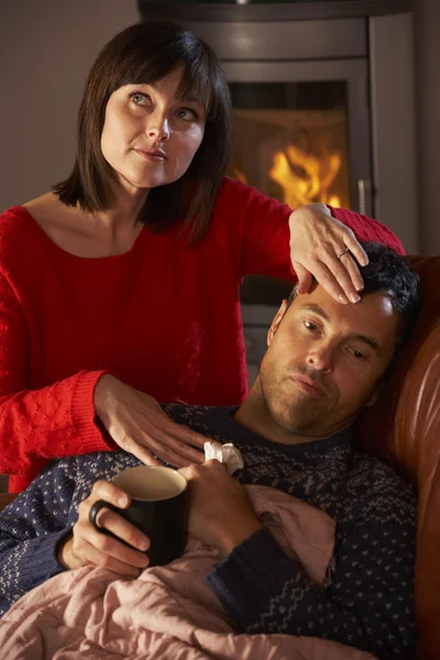 Esposa que amamenta o marido doente com descanso frio no sofá por log acolhedor — Fotografia de Stock